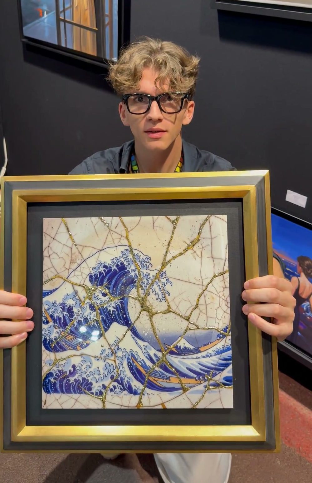 William San holds the kintsugi Great Wave off Kanagawa in both hands, in its black and gold frame, on the Atelier Joconde stand.